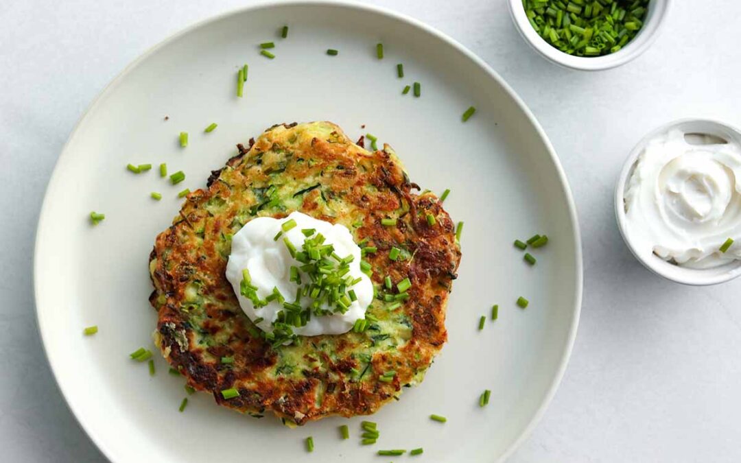 over head view of zuchini fritters with a dollop of dairy free sour cream placed on a ceramic plate and sprinkled with chives