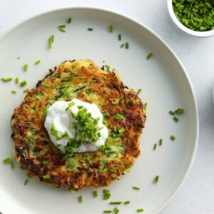 over head view of zuchini fritters with a dollop of dairy free sour cream placed on a ceramic plate and sprinkled with chives