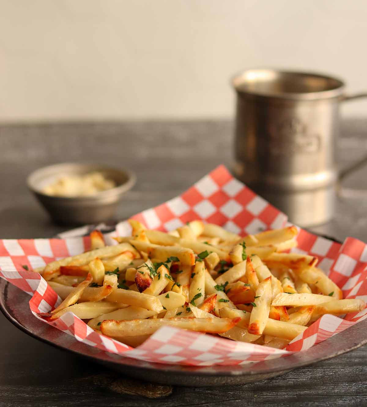 Close up side view of truffle fries served with classic red and white checkered parchment paper with dip and a metal mug in the back ground