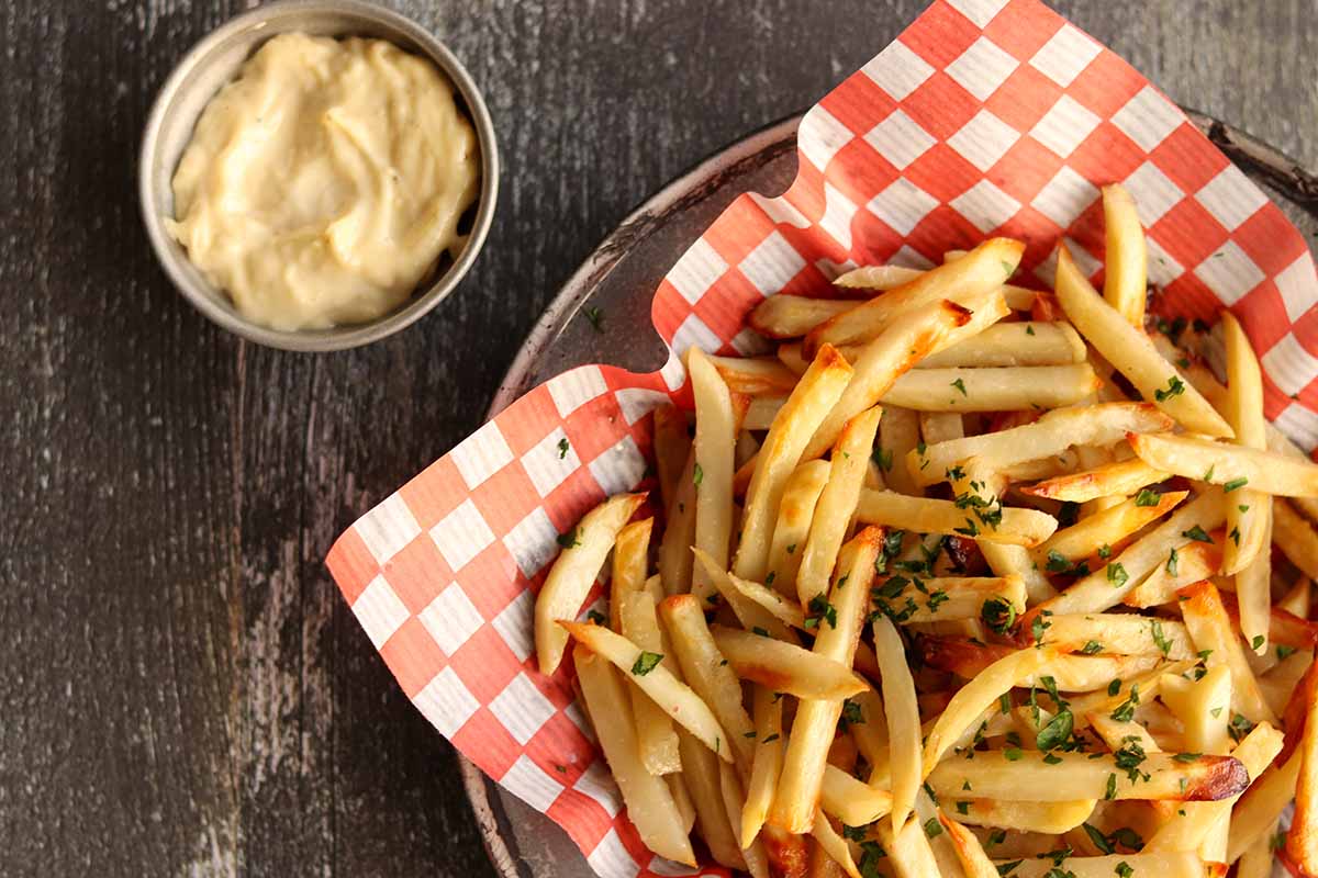 Close up overhead view of truffle fries served on classic checkered paper with a side of dip