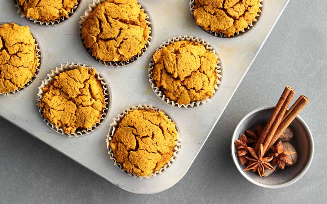 Pumpkin muffins in muffin tin beside a bowl of spices
