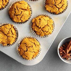 Pumpkin muffins in muffin tin beside a bowl of spices