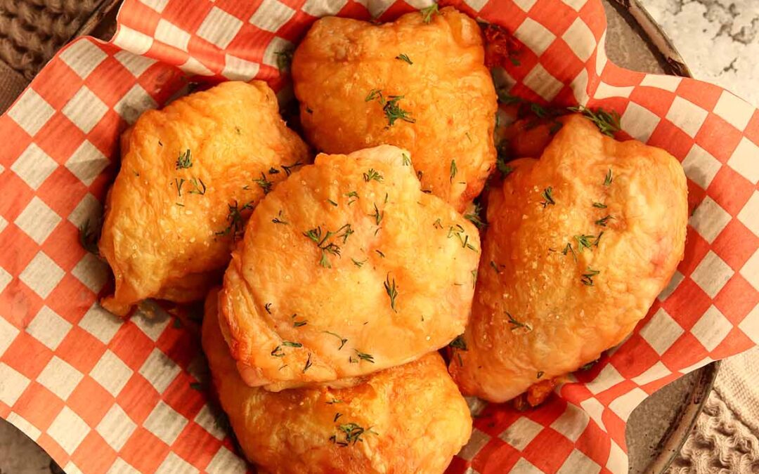 Overhead view of crispy chicken thighs served in white and red checkered parchment paper