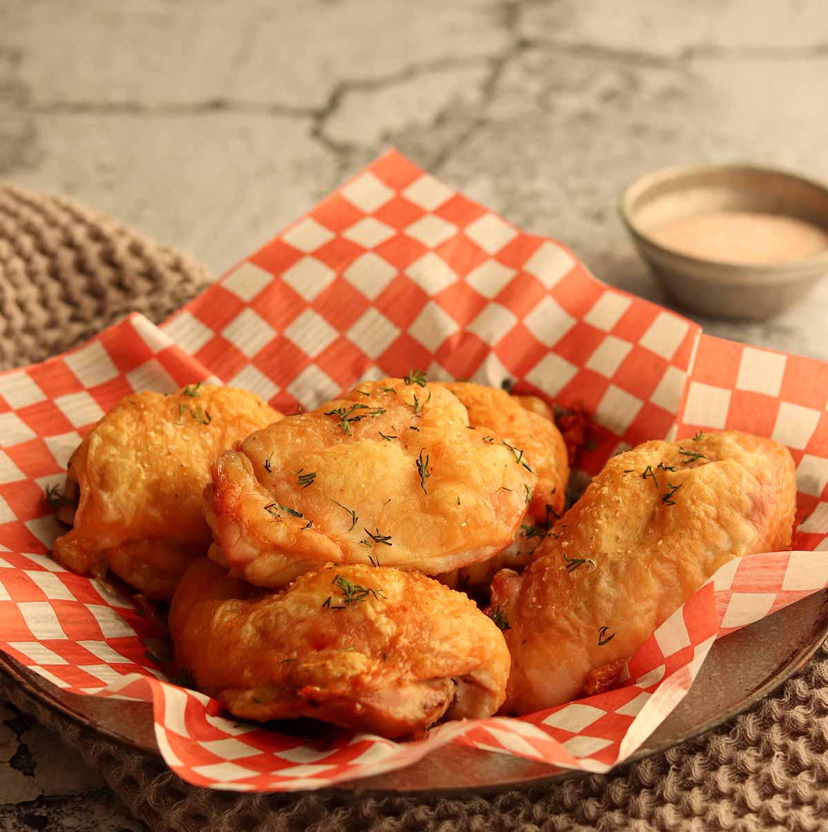 Side view of crispy oven baked chicken thighs placed in white and red checkered parchment paper