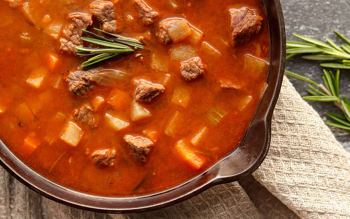 Close up view of beef stew in a cast iron skillet topped with fresh herbs