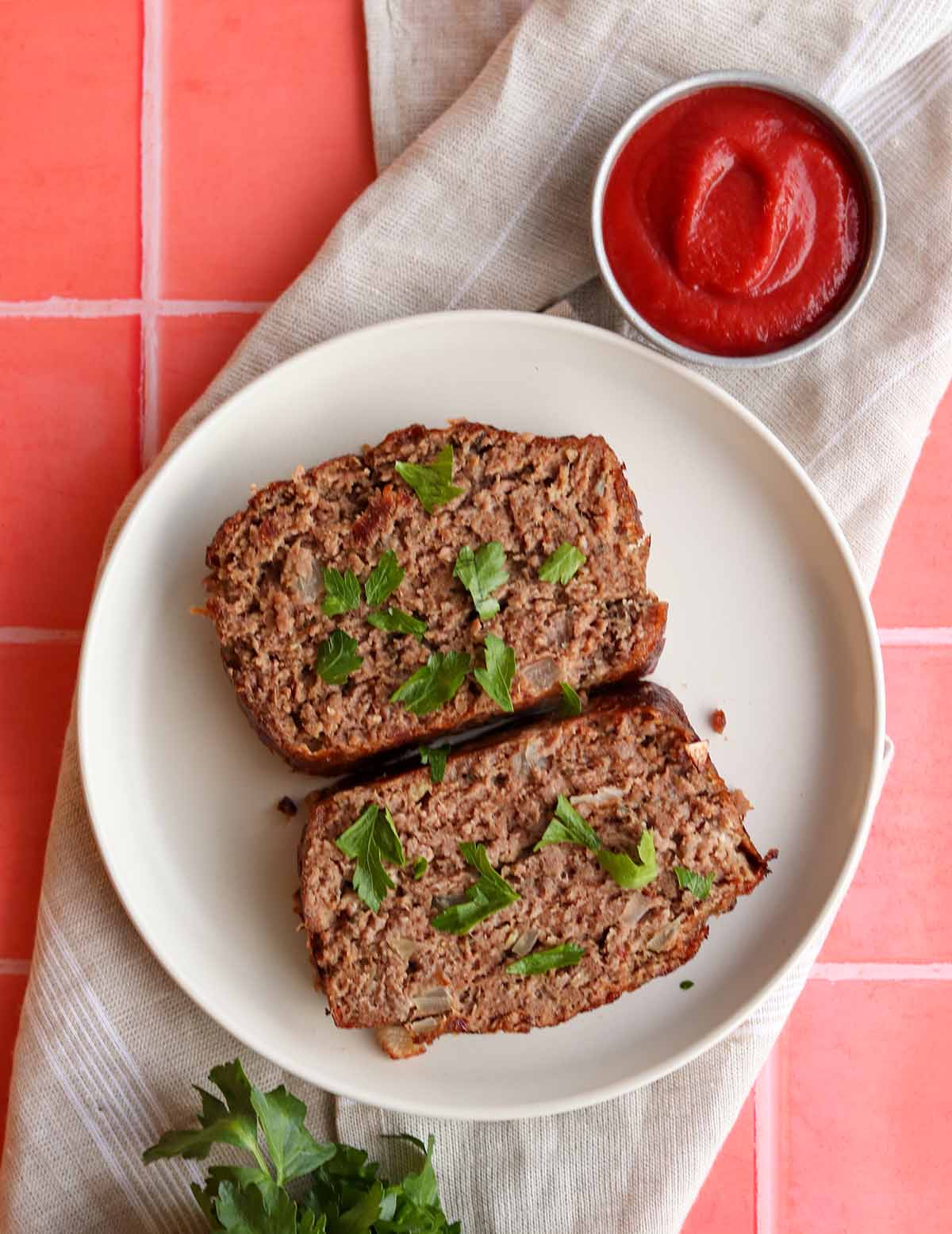 Overhead view of paleo meatloaf slices on a white plate beside a a ramekin of ketchup