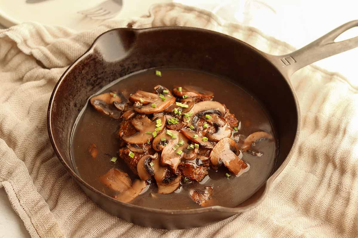 Close up view of Salisbury steak in a skillet topped with sautéed mushrooms