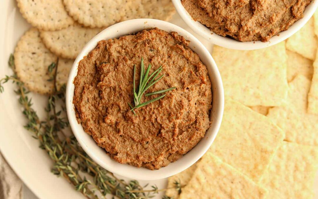 Close up view of beef liver pate in a white ceramic container surrounded by crackers and garnish