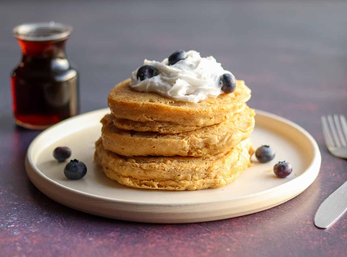 Fluffy oat flour pancakes stacked high with toppings and syrup in the background