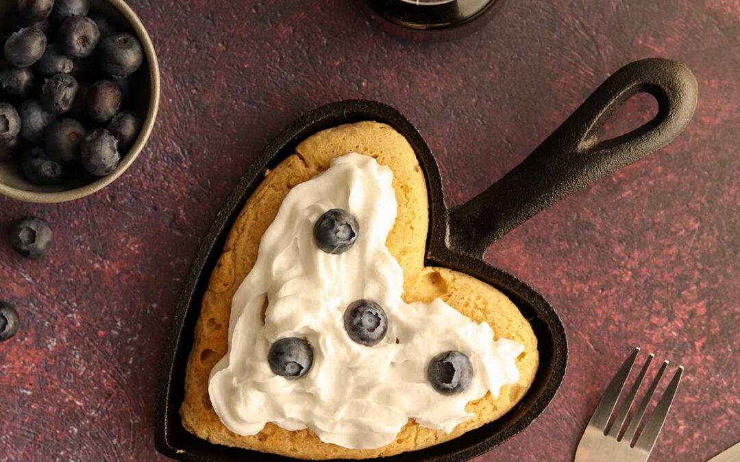 Oat flour pancake in a heart shaped cast iron skillet with whip cream and toppings