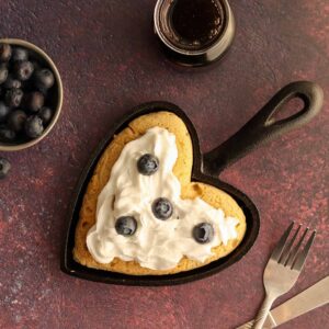 Oat flour pancake in a heart shaped cast iron skillet with whip cream and toppings