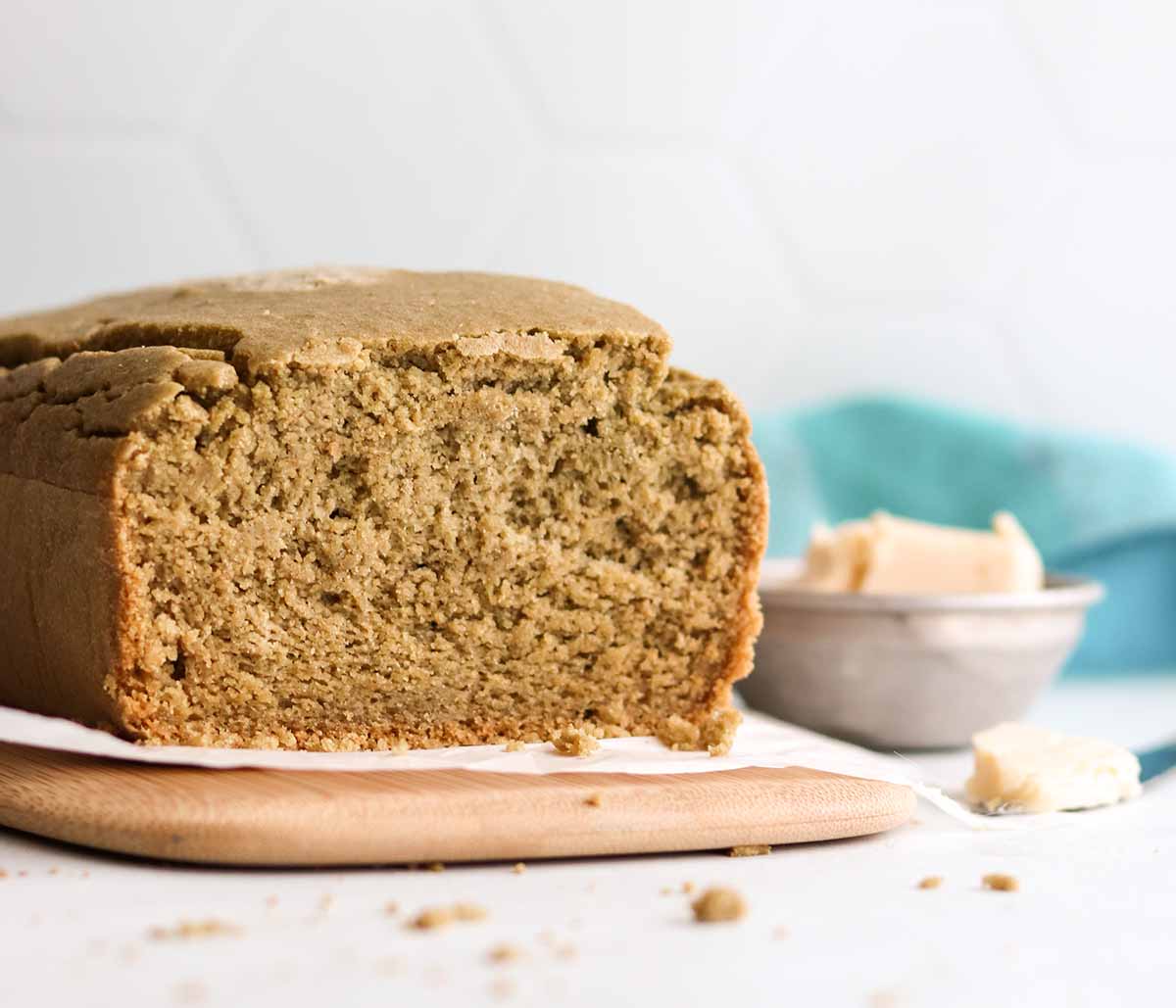 Close up view of sliced oat flour bread placed on top of parchment paper sitting on a wooden cutting board beside a bowl of butter