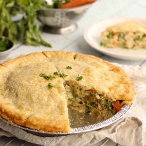 Whole gluten free dairy free chicken pot pie with slice missing exposing the tasty and colourful filling. topped with chives.
