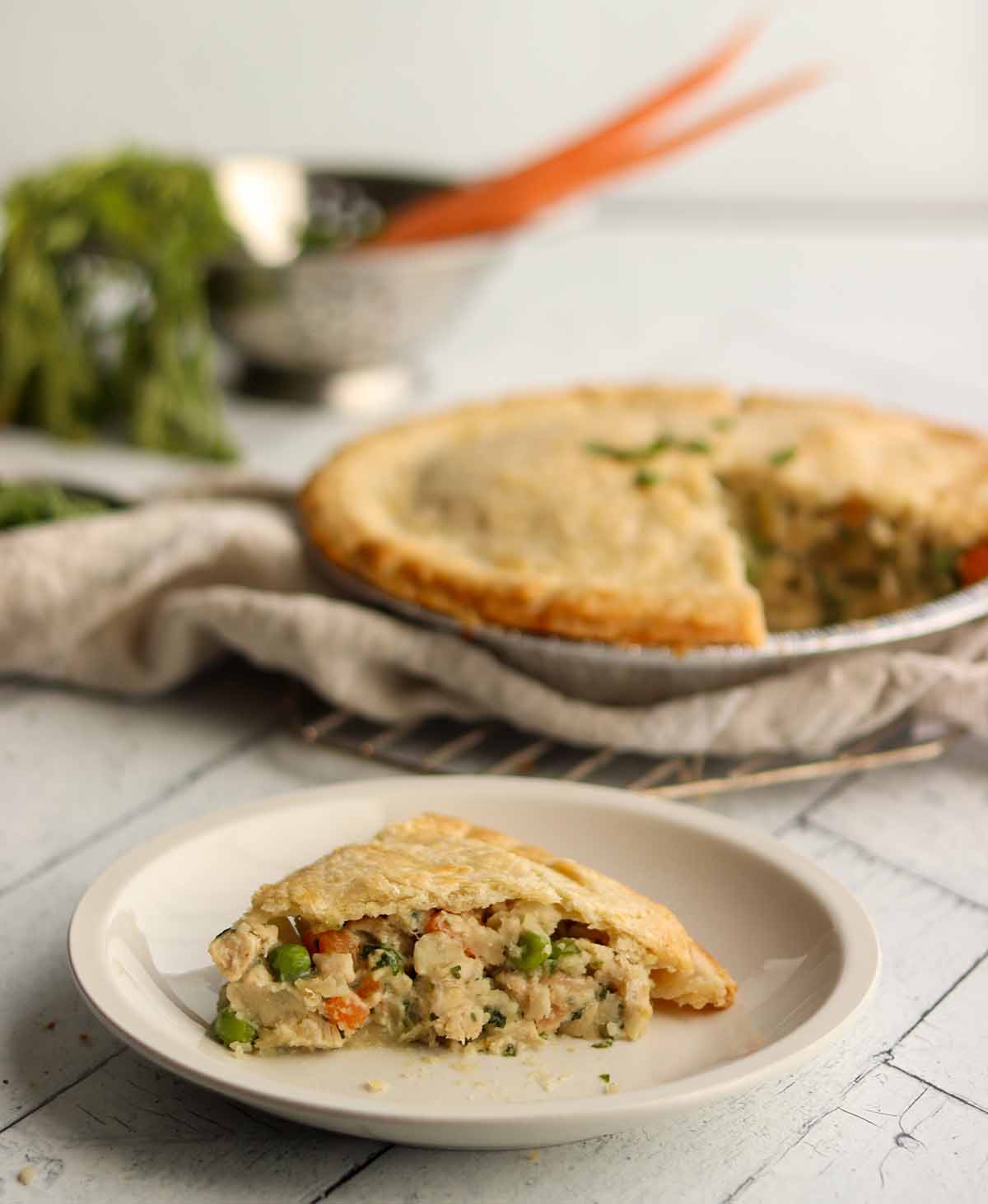 Gluten free dairy free chicken pot pie slice on a place with whole pie in background. Surrounded by fresh ingredients and linen cloth.