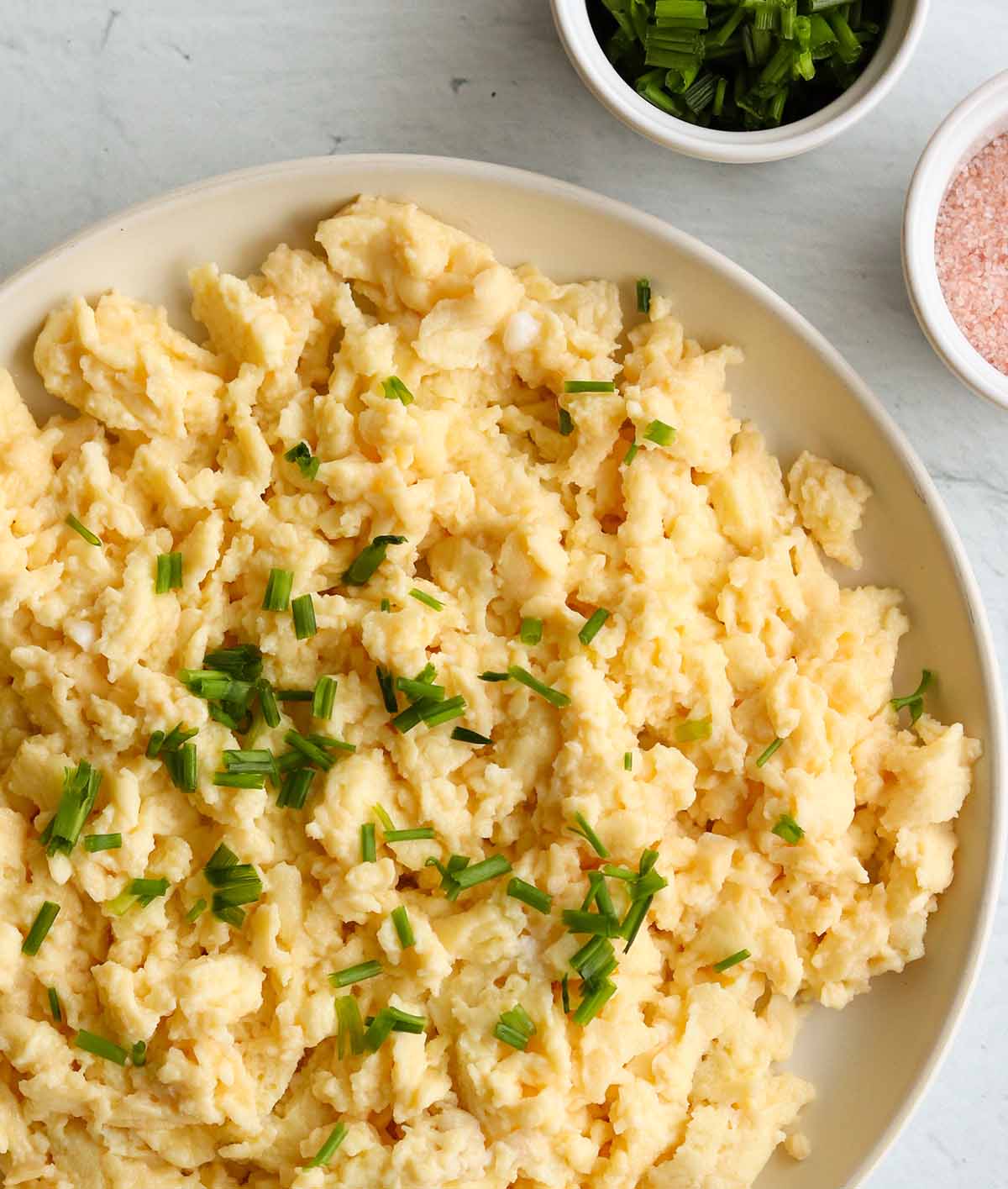 Close up view of dairy free scrambled eggs topped with green garnish surrounded by ingredients. 