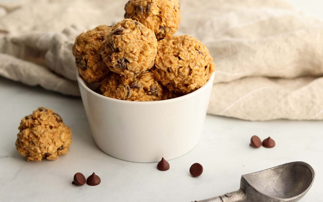 Edible cookie dough scooped into round balls placed in a white ceramic dish surrounded by chocolate chips.