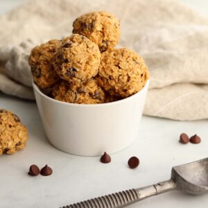 Edible cookie dough scooped into round balls placed in a white ceramic dish surrounded by chocolate chips.