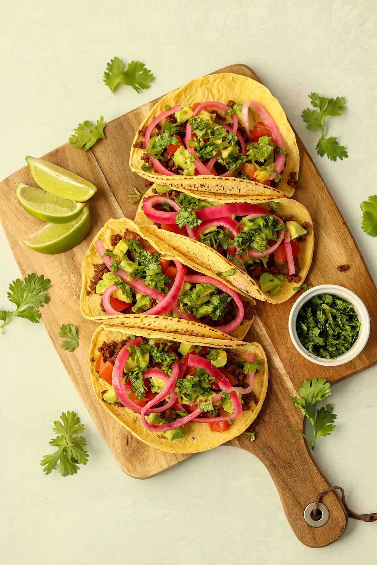 Zoomed out overview of bison tacos lined up on wooden serving platter surrounded by brightly coloured garnish.