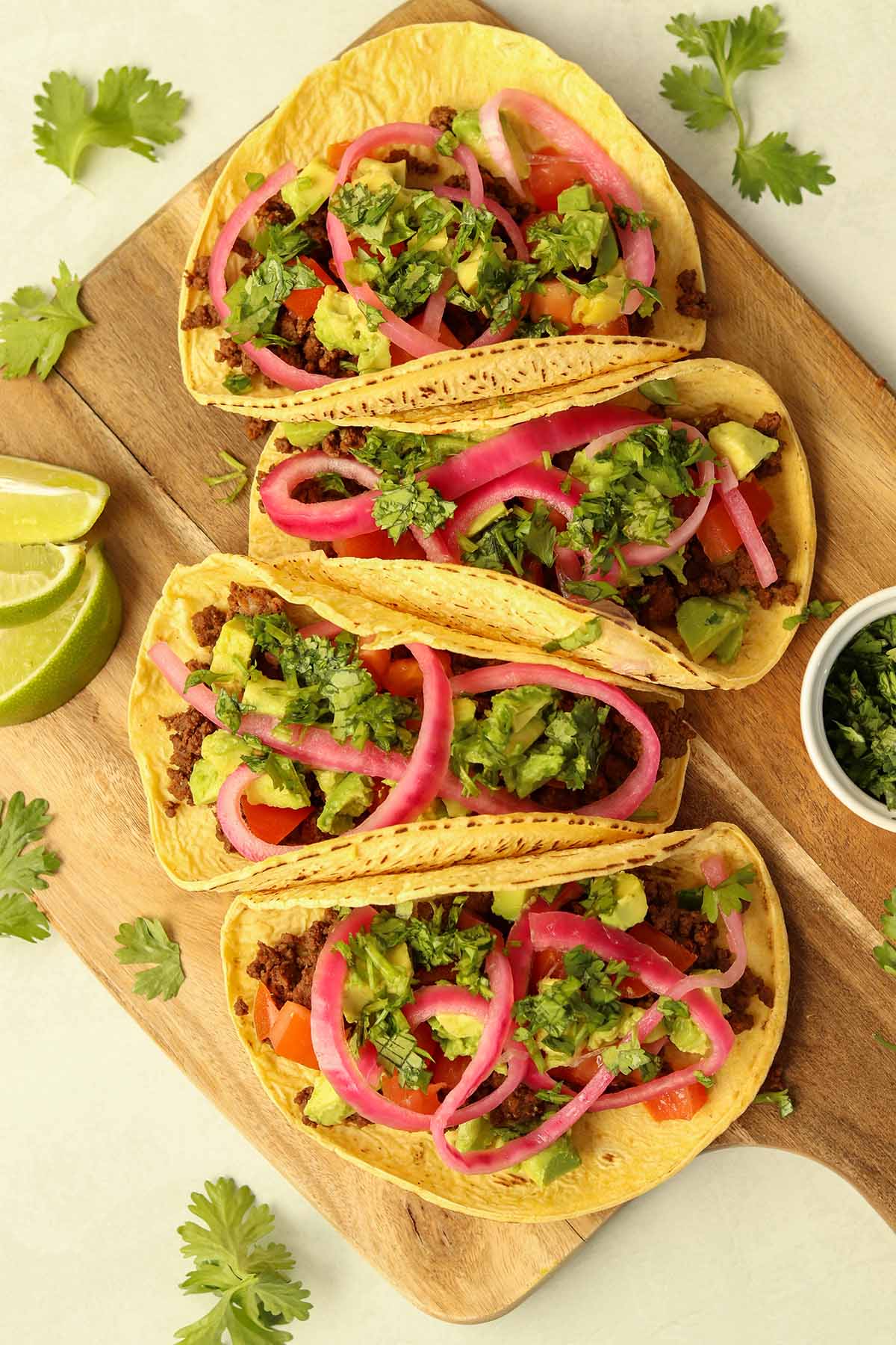 Overhead view of bison tacos lined up on wooden serving platter surrounded by brightly coloured garnish.