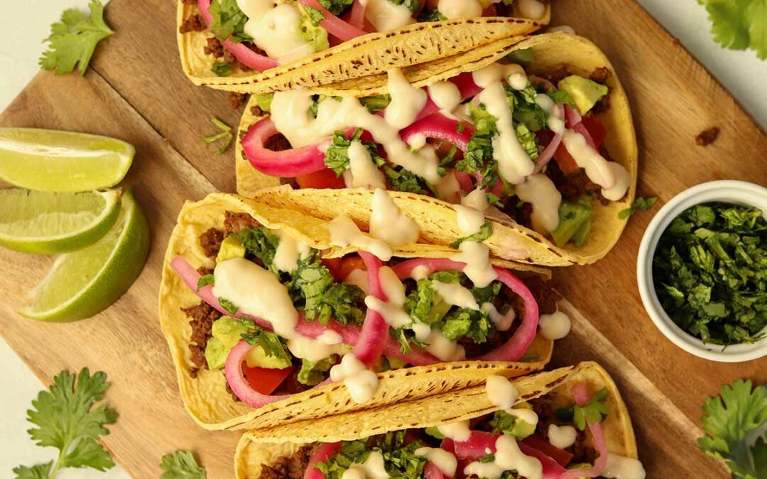 close up overview of bison tacos lined up on wooden serving platter surrounded by brightly coloured garnish.