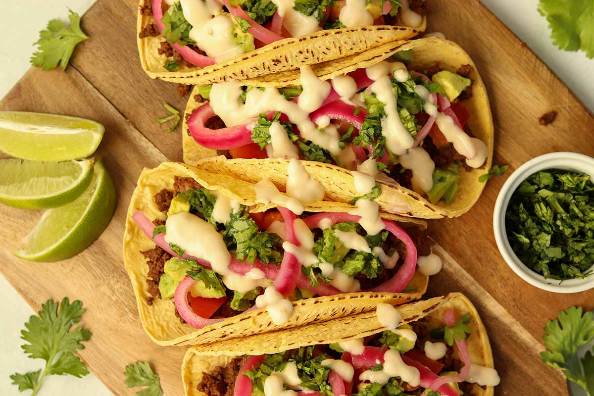 close up overview of bison tacos lined up on wooden serving platter surrounded by brightly coloured garnish.