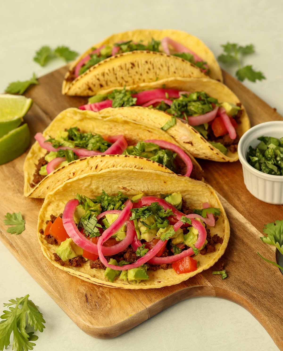 Close up side view of bison tacos lined up on wooden serving platter surrounded by brightly coloured garnish.