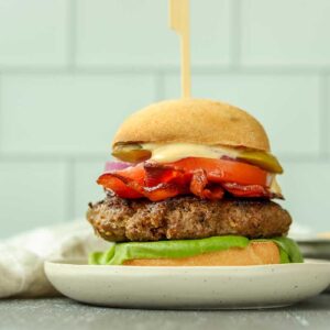 Close up bottom view of fully stacked moose burger on a white plate surrounded by a clothe and a ramekin of sauce