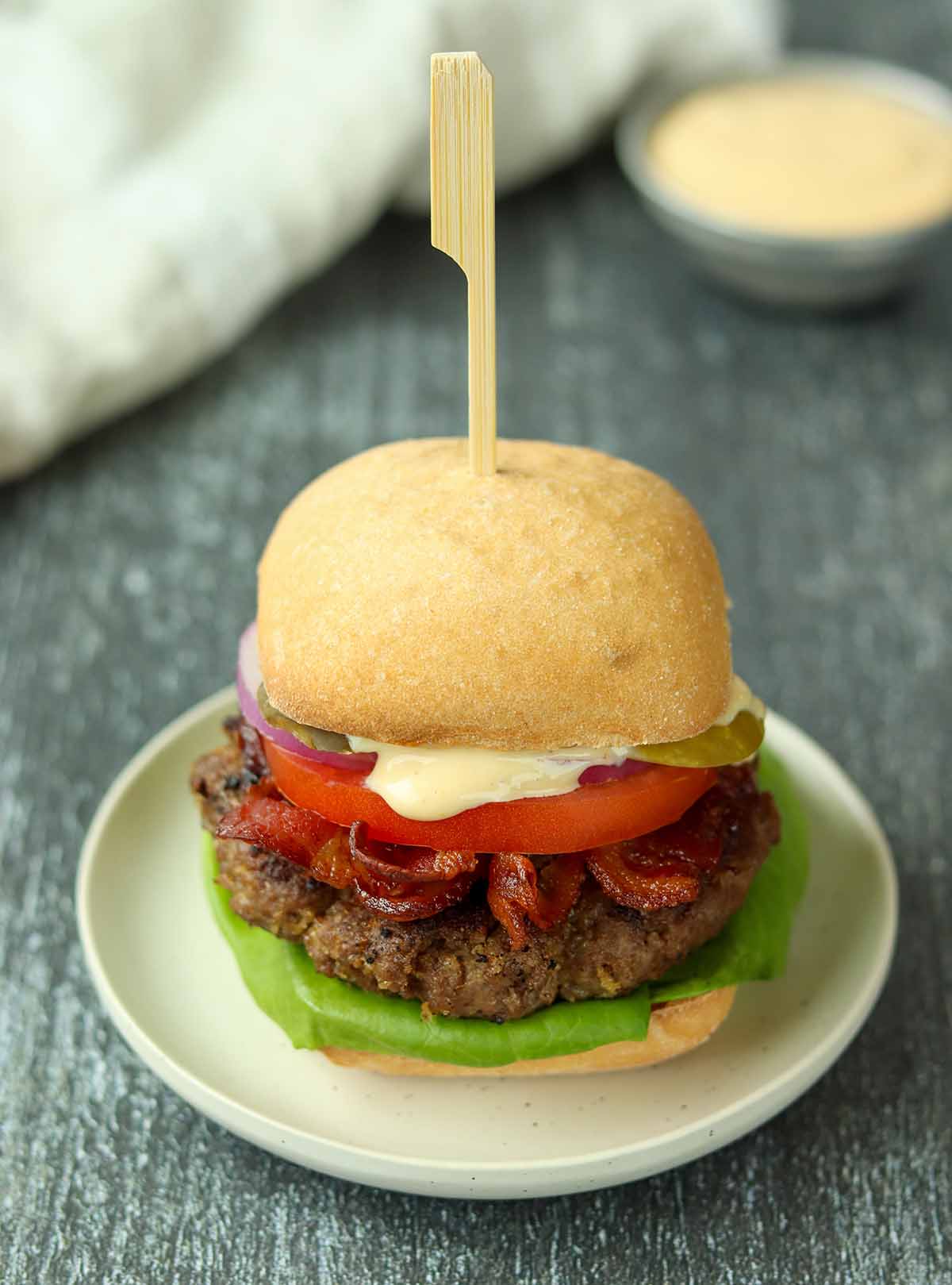 Close up view of moose burger on a white ceramic plate placed on top of a wooden table.