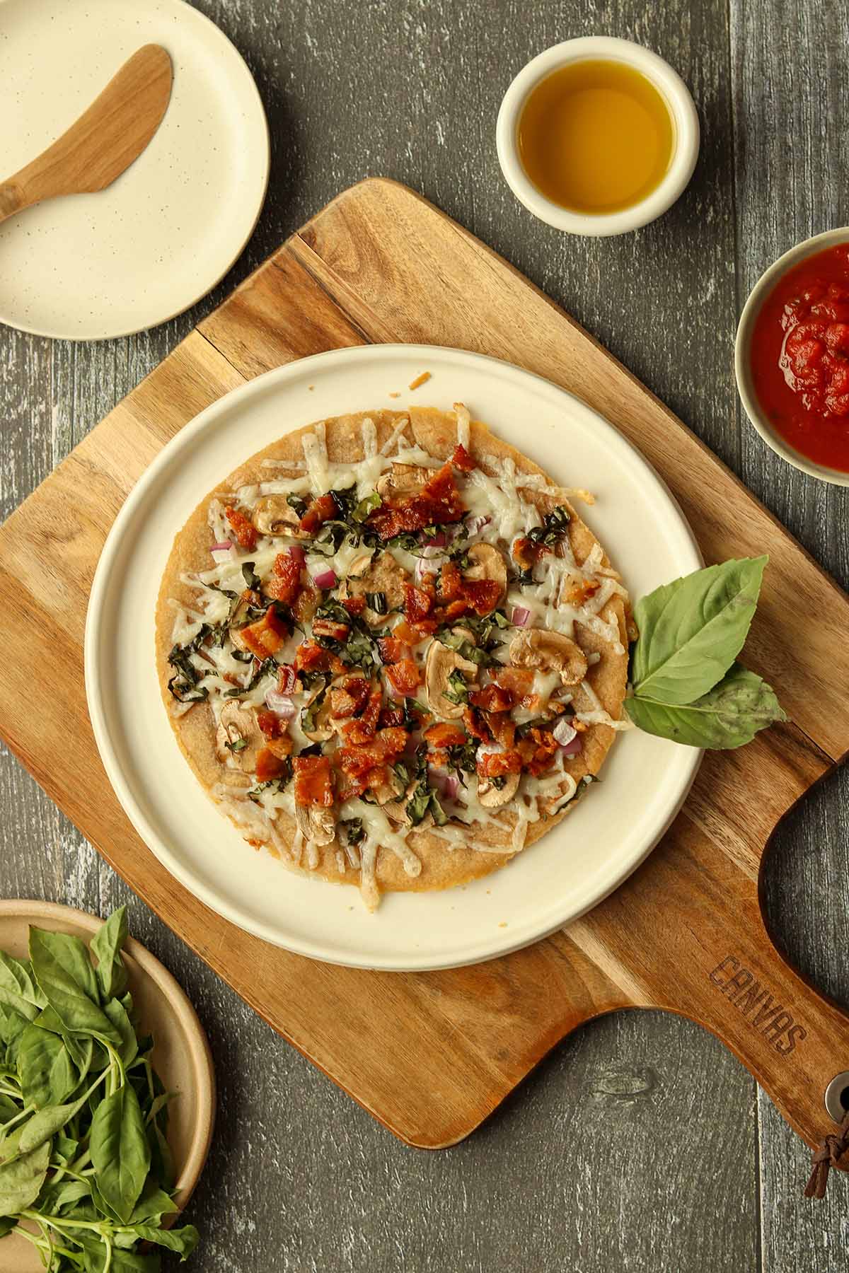 Zoomed out view of fully loaded cassava flour pizza surrounded by fresh ingredients and sauces.