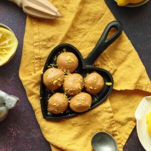 Zoomed out overhead view of collagen balls in a heart shaped cast iron skillet surrounded by ingredients and placed onto a yellow kitchen towel.