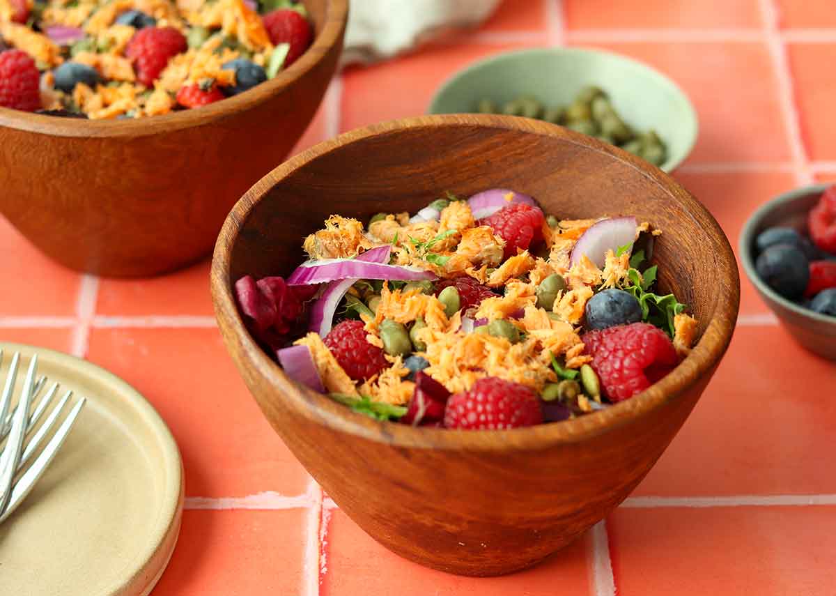 Side view of two wooden bowls with a colourful smoked salmon salad inside.